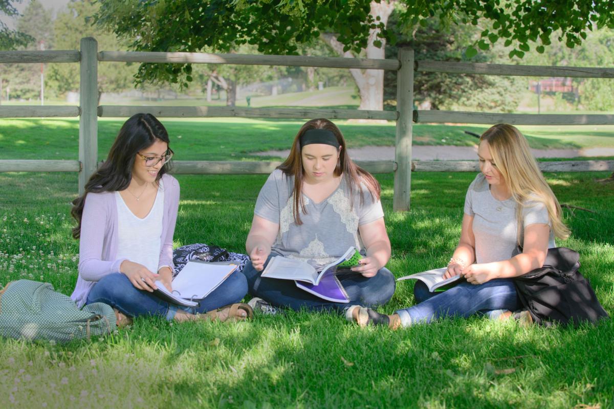 3 female students studying together while seated on the grass