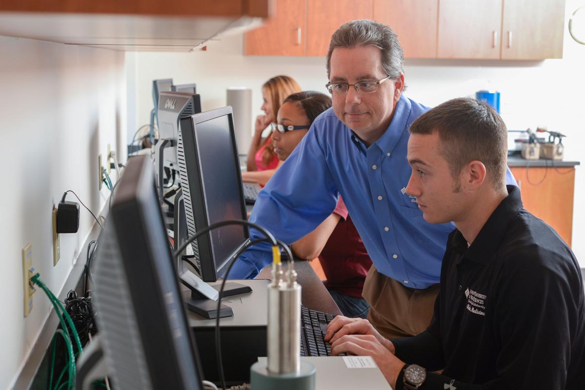 A male nuclear medicine student using lab equipment while a faculty member observes