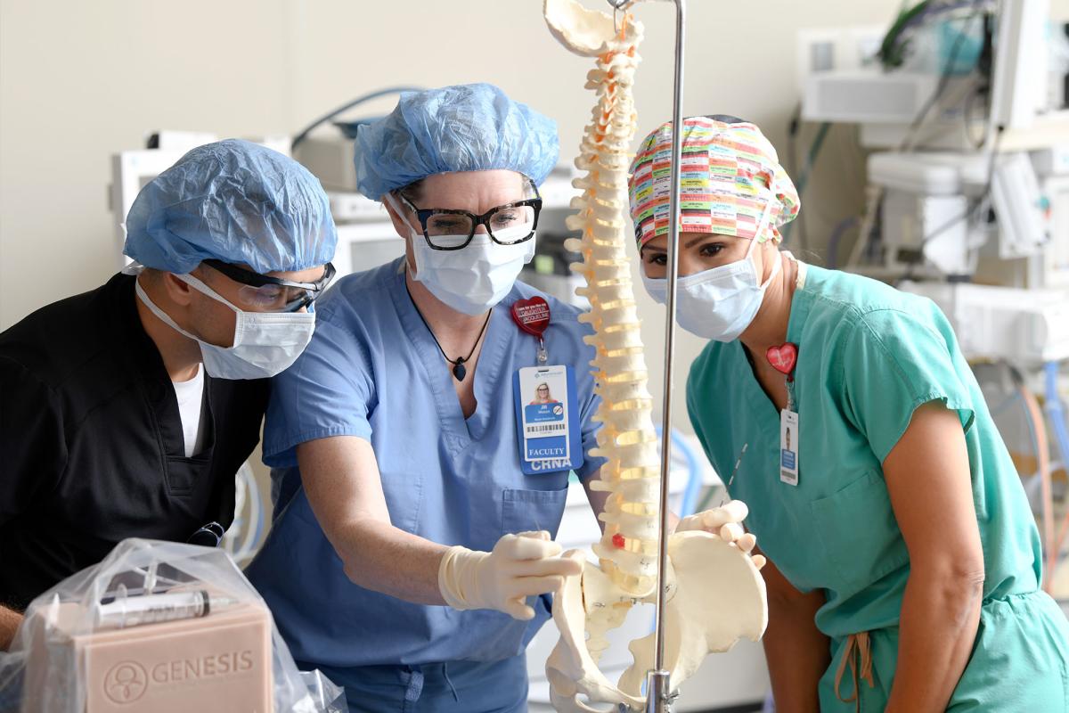 A faculty member demonstrates a procedure on the spine for students in the skills lab
