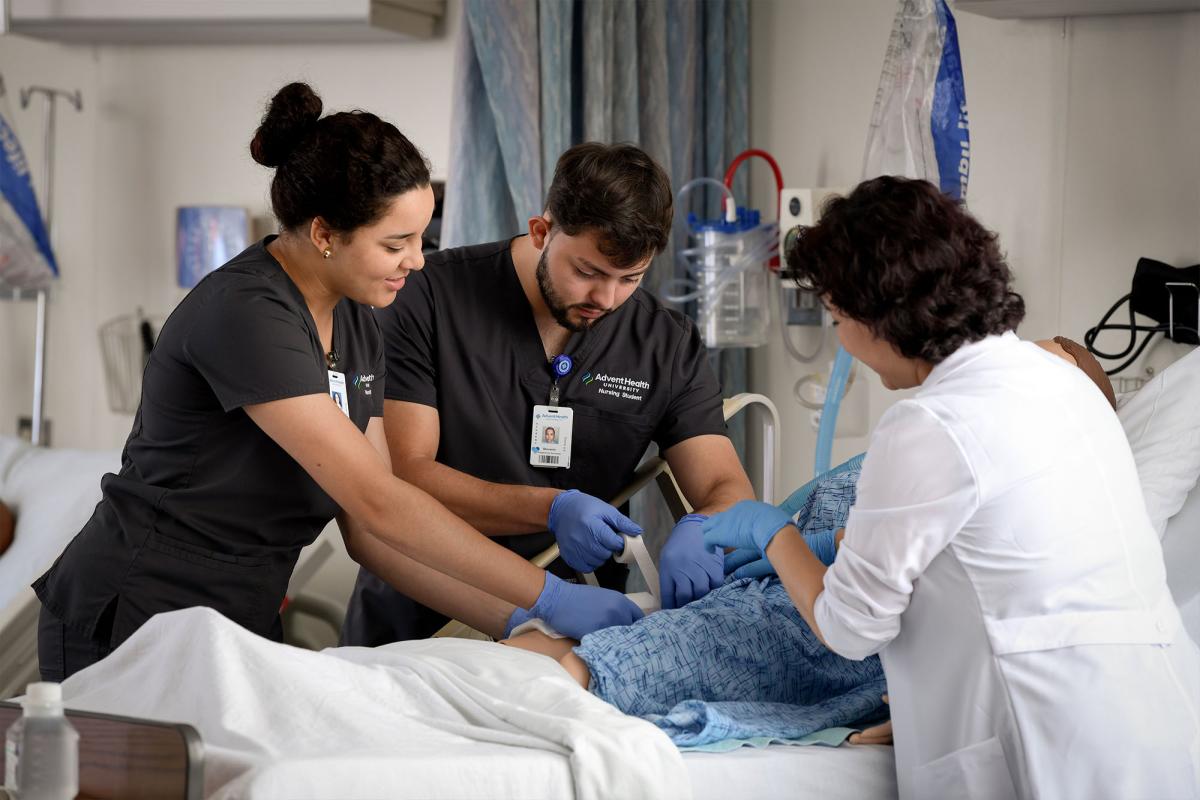 Two nursing students practice their skills on a simulator with faculty guidance.