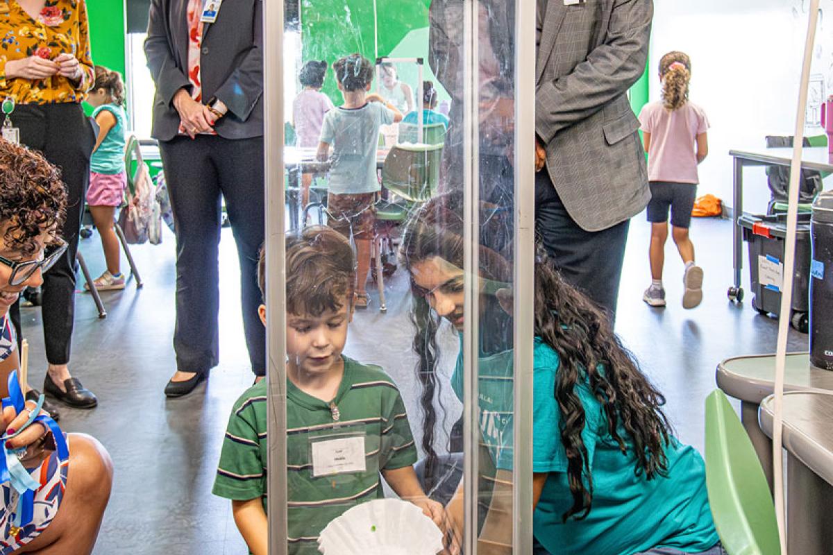 Ruben Martinez smiles and looks at little boy conducting experiment
