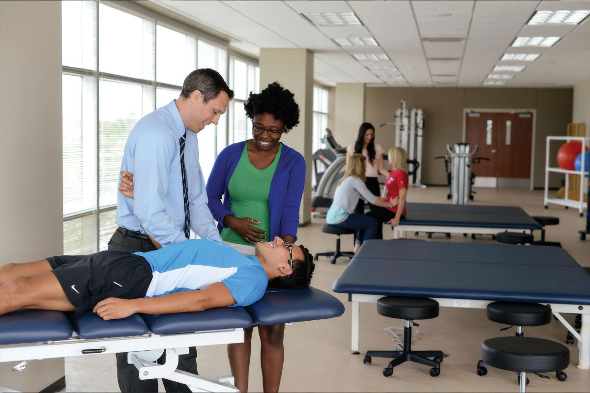 Physical therapy faculty demonstrates shoulder therapy on a student while another observes