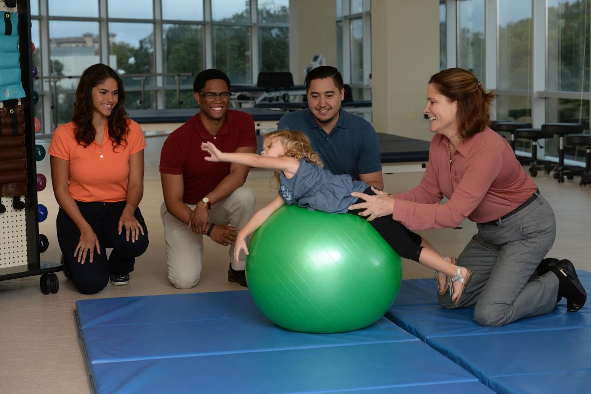 A physical therapy teach demonstrates therapy on a child to a group of students