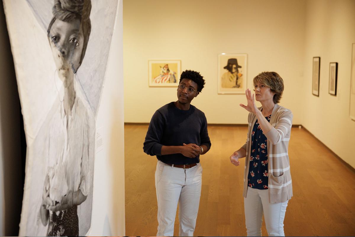 A faculty and student discuss artwork in a museum
