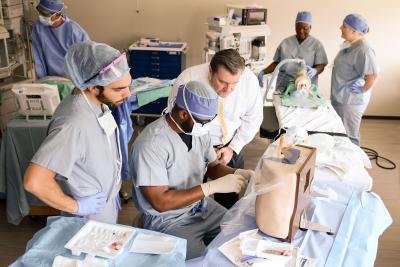 A professor supervises nurse anesthesia students in performing a spine injection on a simulator