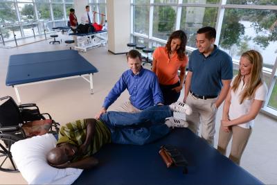 A professor demonstrates therapy techniques on a patient to a group of students