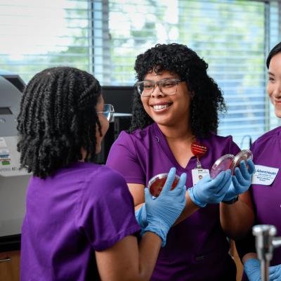 Three medical lab sciences students wearing scrubs practicing their skills using lab equipment.
