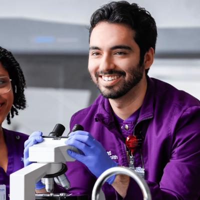 a male and a female medical lab science student practicing microscope skills in a lab