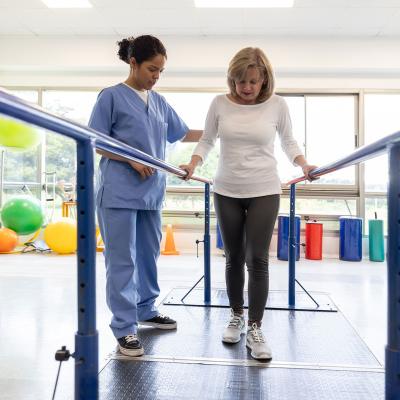 A physical therapist works with a patient who is using parallel bars