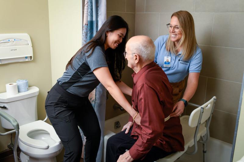 Image of faculty member smiling and helping patient with a student