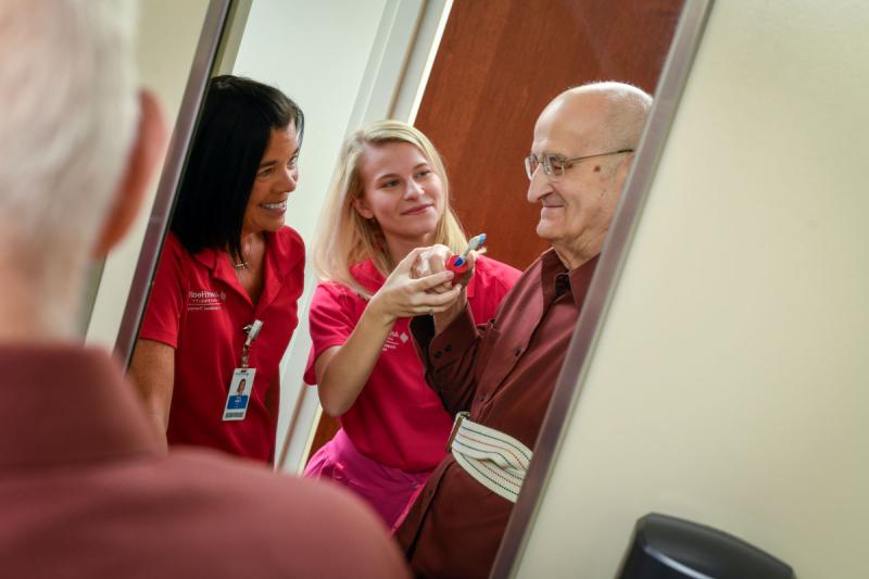 Image of faculty member smiling and helping patient with a student