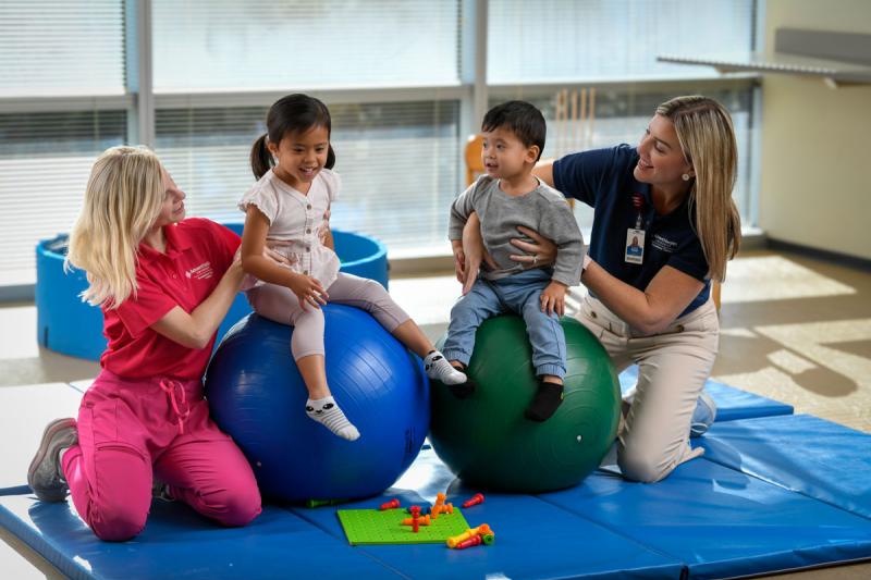 Image of faculty member smiling and helping two pediatric patients with a student.