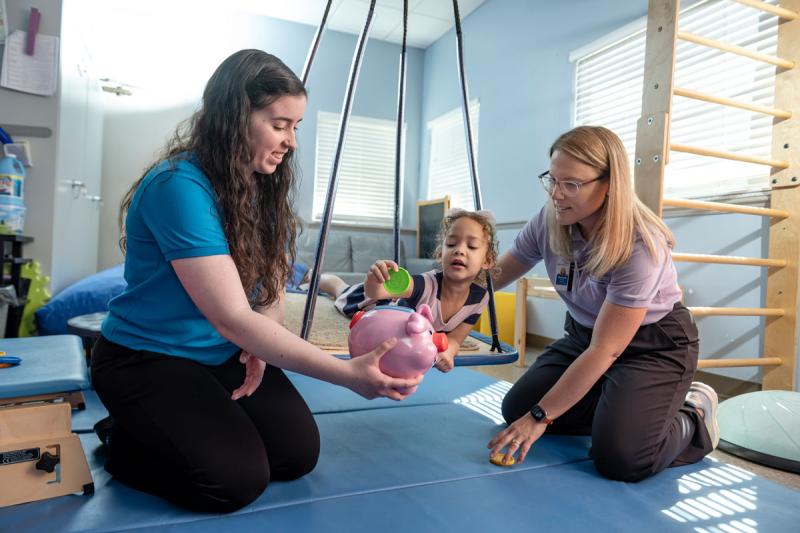 Image of faculty member smiling and helping pediatric patient with a student