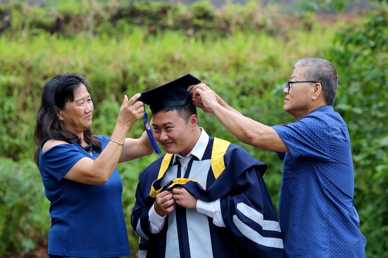 Parents help a graduate get dressed in cap and gown