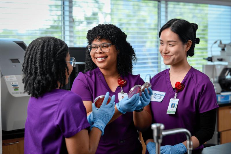 Three medical lab sciences students wearing scrubs practicing their skills using lab equipment.