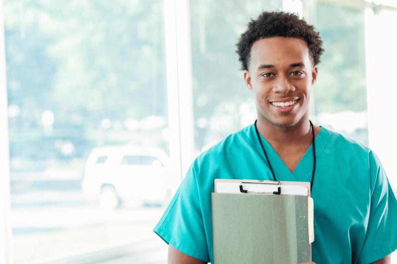 A smiling Male nurse holding a clipboard.