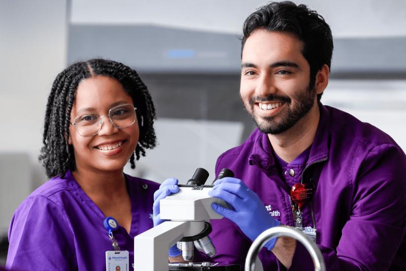 a male and a female medical lab science student practicing microscope skills in a lab