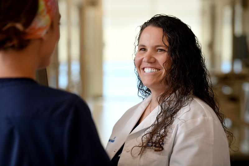 A nurse in a white coat smiling and talking with another nurse