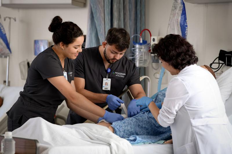 Two nursing students practice their skills on a simulator with faculty guidance.