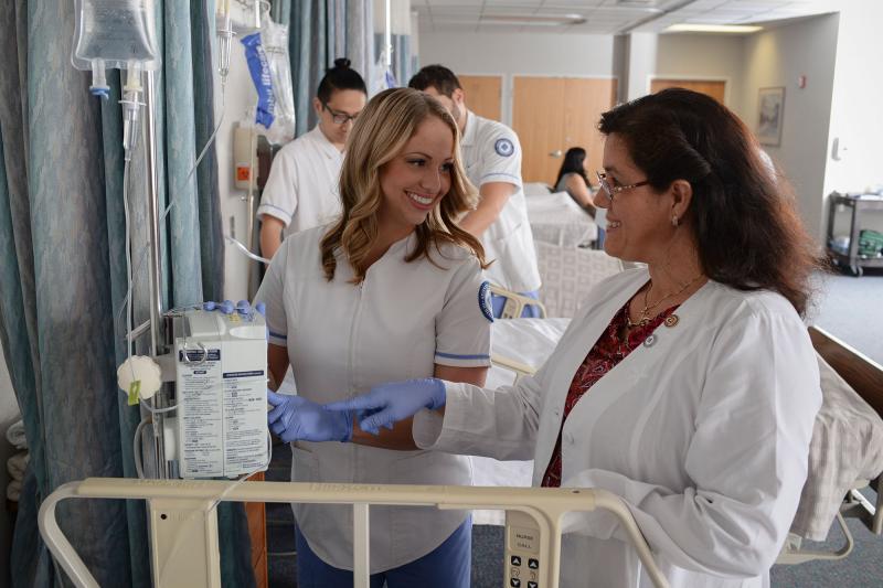 A nursing faculty member supervising a student in the nursing skills lab