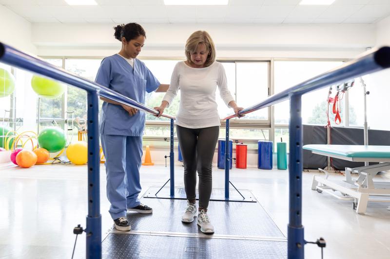 A physical therapist works with a patient who is using parallel bars