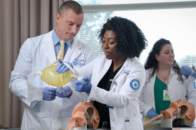 A physician assistant practices intubation on a simulator under faculty supervision