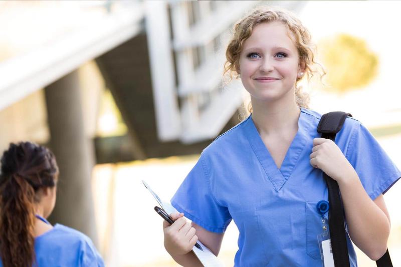 A young nurse in scrubs walks with a backpack