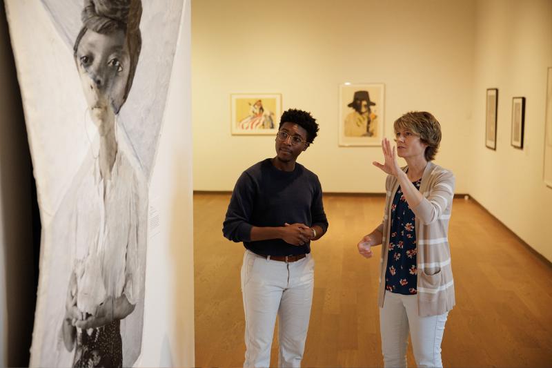 A faculty and student discuss artwork in a museum
