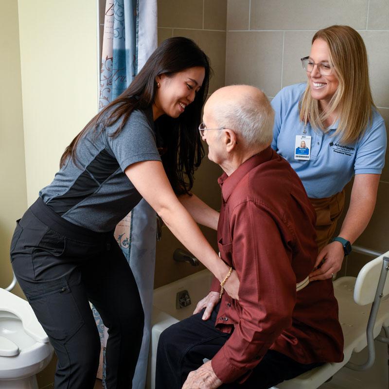 Image of faculty member smiling and helping patient with a student