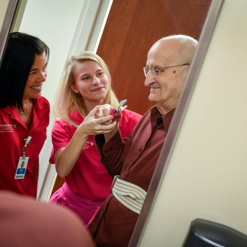 Image of faculty member smiling and helping patient with a student