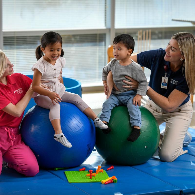 Image of faculty member smiling and helping two pediatric patients with a student.