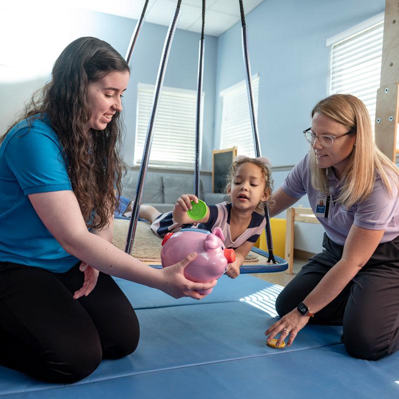 Image of faculty member smiling and helping pediatric patient with a student