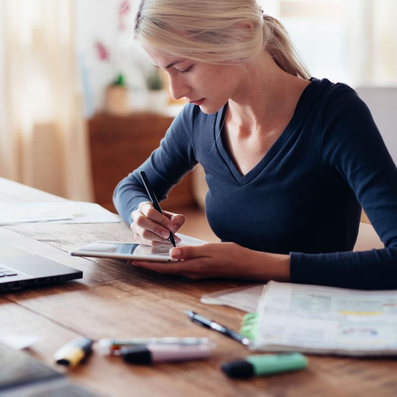 A Woman Writes on Her Tablet at Her Desk