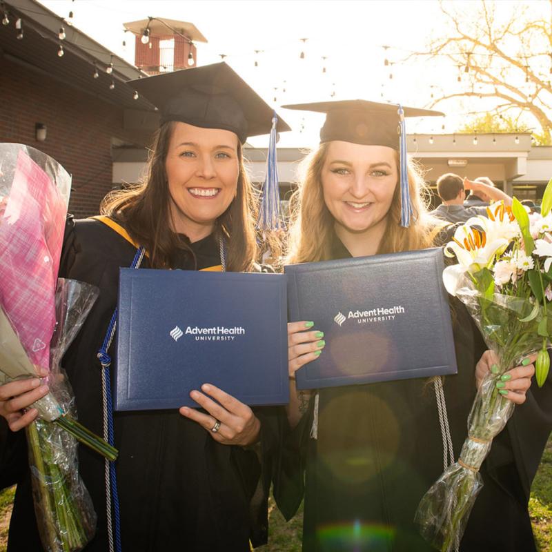 Two graduates of AHU Denver pose with their diplomas