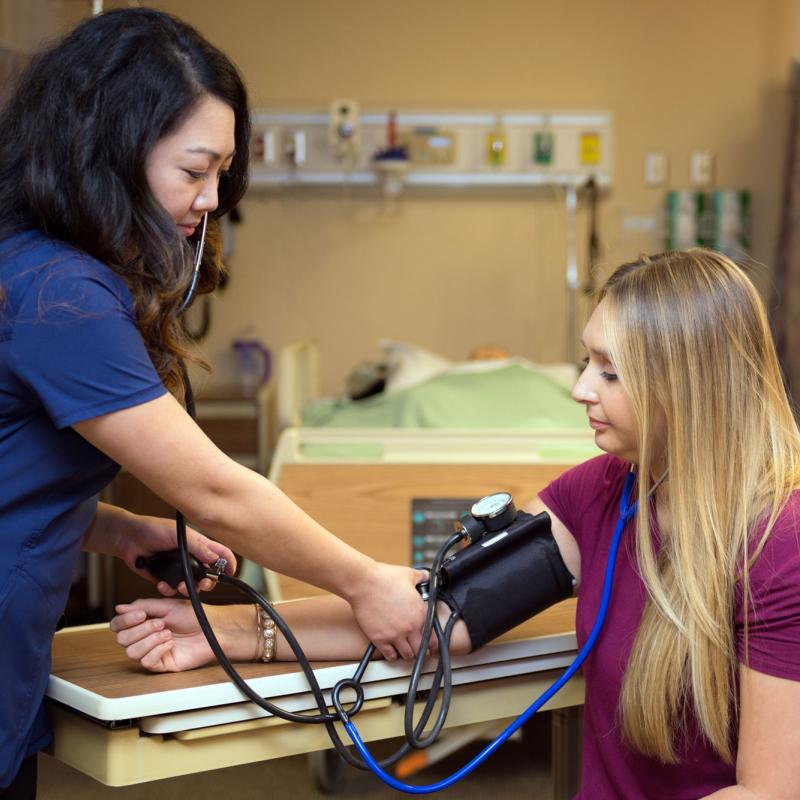 A female nursing student taking a blood pressure reading of another student