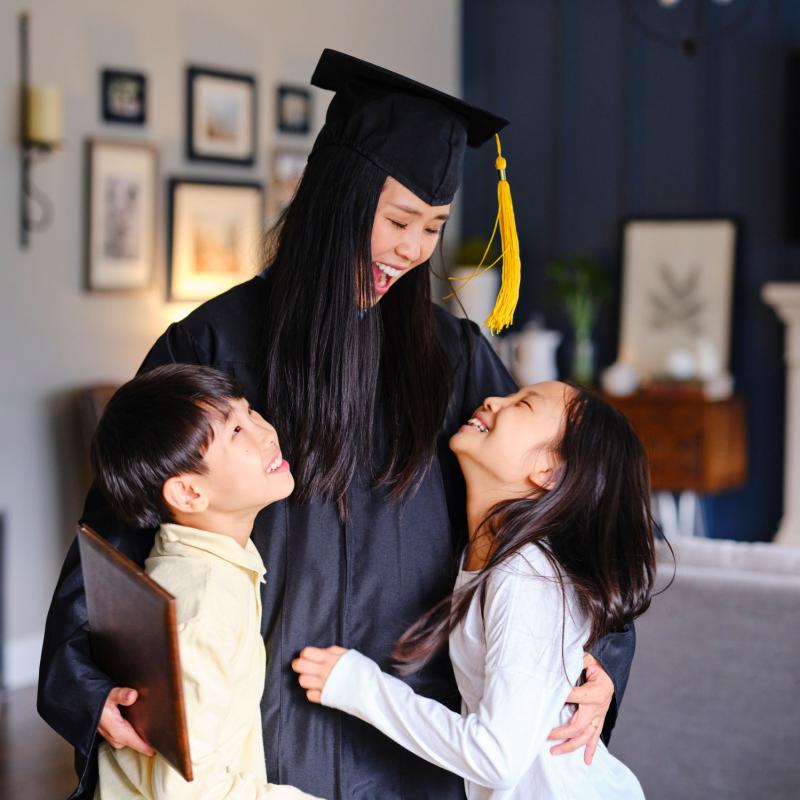 A female graduate laughs and hugs her children at home