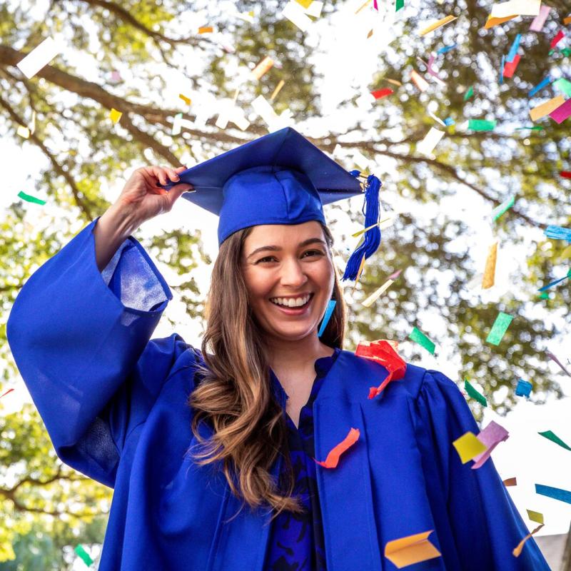 A young female graduate smiling as confetti drops around her