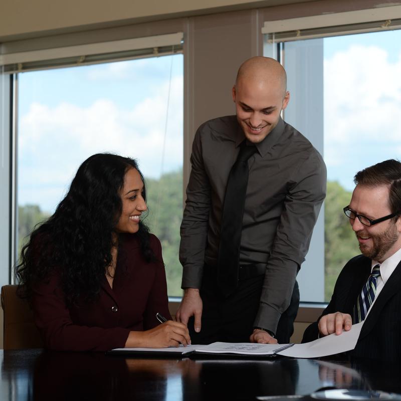 A professor teaches two students at a conference table