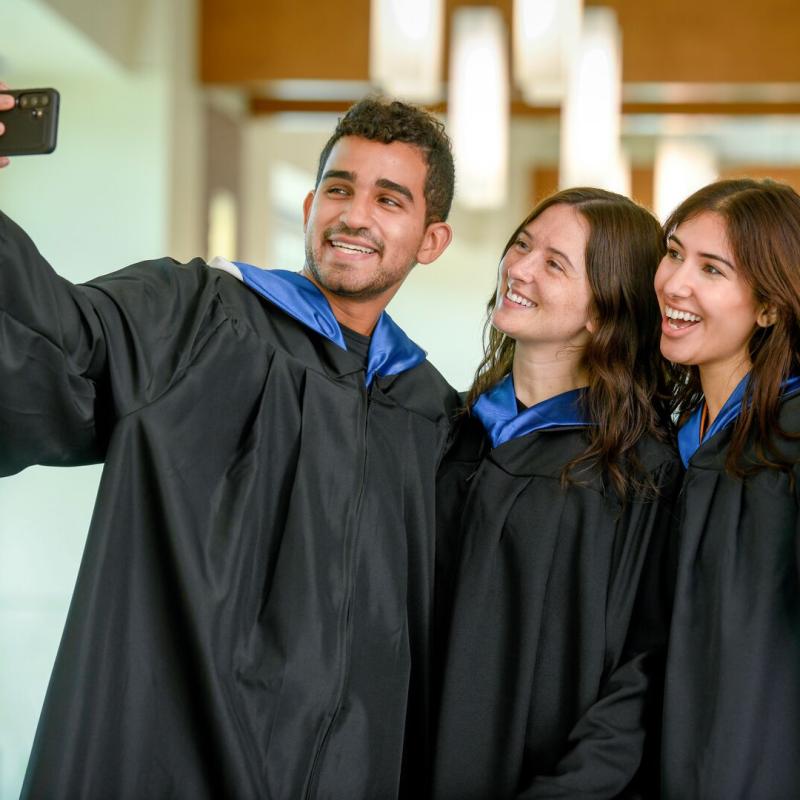 Three graduates smiling in regalia