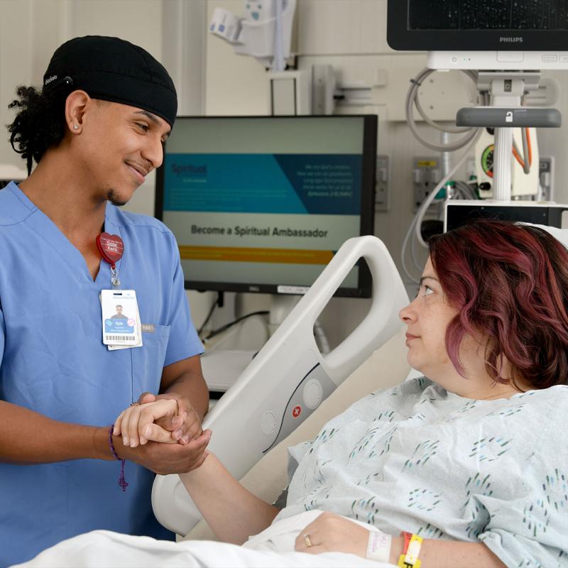 A nurse comforts a patient and holds their hand