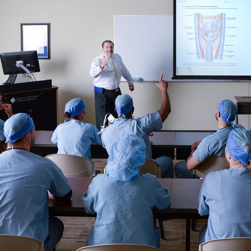 A faculty member lecturing and presenting a slideshow to nurse anesthesia students
