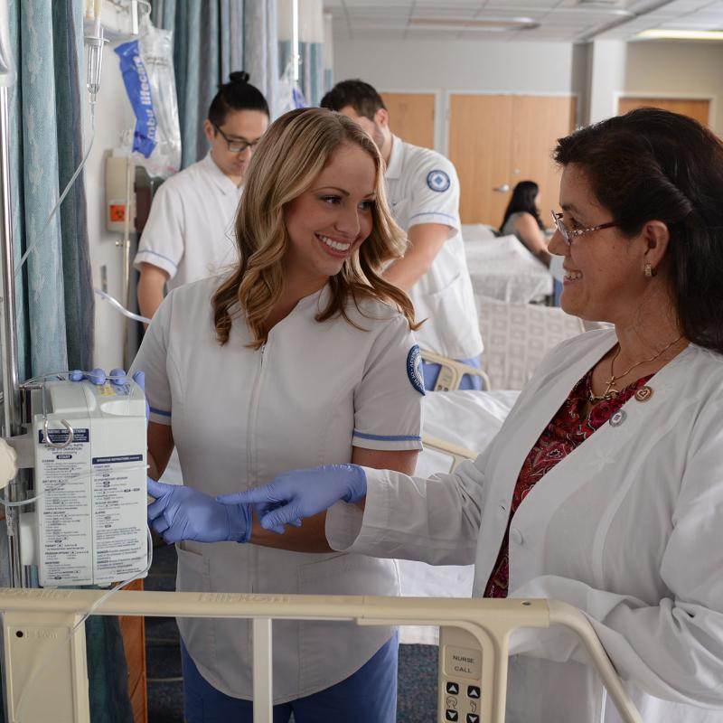 A nursing faculty member supervising a student in the nursing skills lab