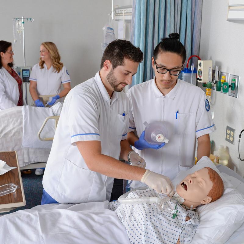 Two nursing students practice their skills in the lab using a patient simulator