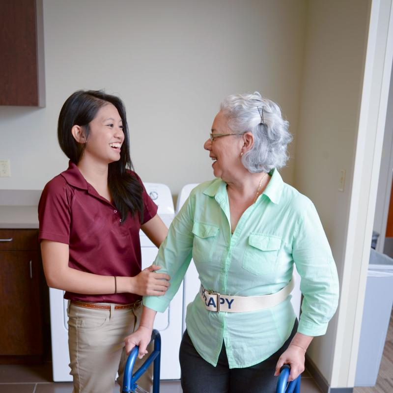 An occupational therapy student works with an elderly patient using a walker