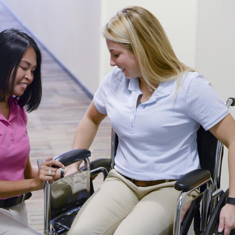 Two female occupational therapy students practicing skills in a wheelchair