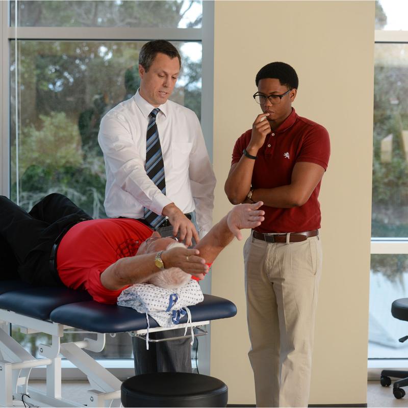 A physical therapy student observing a faculty member provide care to a patient