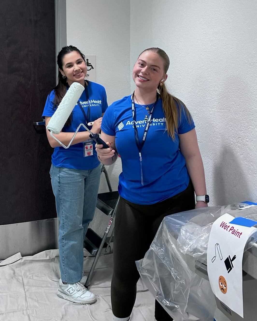 Two students smiling and painting for all AHU service day