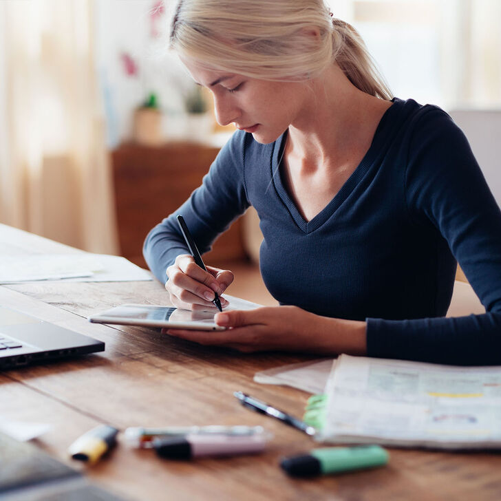 A Woman Writes on Her Tablet at Her Desk