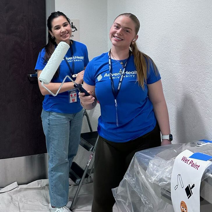 Two students smiling and painting for all AHU service day