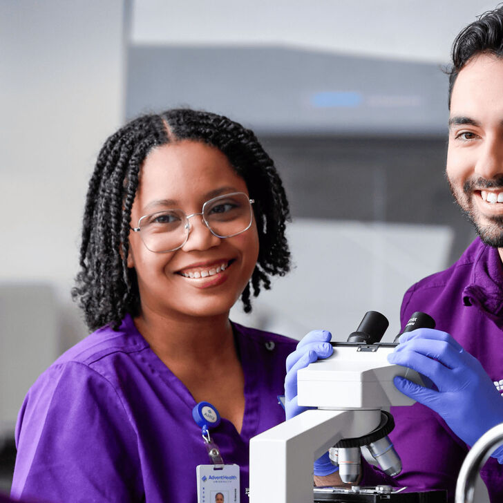 a male and a female medical lab science student practicing microscope skills in a lab